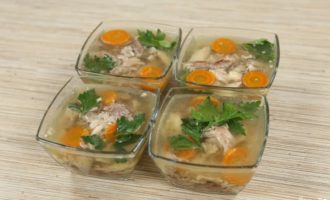 Preparing the molds for the filling. It’s better if these are small transparent bowls, then all the beauty will be clearly visible. Cover the bottom of the bowls with a small amount of broth, place a composition of chicken fillet, carrots and parsley leaves on top, then pour the remaining broth into the bowls.Before putting the aspic in the refrigerator, make sure it has cooled to room temperature.