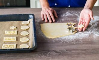 Cut out cookies from the prepared shortbread dough using different molds or cups. After this, spread baking paper on a baking sheet and place the cookies on it. 