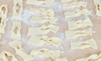 After this time, cut the dough into 2-3 pieces and roll each piece into a sheet up to 2 mm thick. We cut the sheet into rectangles measuring 2x7 cm. We cut each product in the middle and twist one end through the cut. In this way we form products from the entire dough.