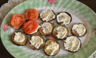 Agora coloque as berinjelas em um prato. Cubra o topo de cada círculo com a mistura de maionese e cubra com tomate. Para beleza, você pode adicionar uma folha de verdura.