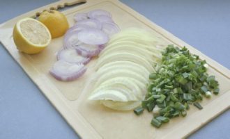 Wash the lemon and cut into thin slices. Peel the onions and cut into half rings, wash the garlic arrows and chop finely. Mix lemon, onion and garlic, salt and sprinkle with pepper.