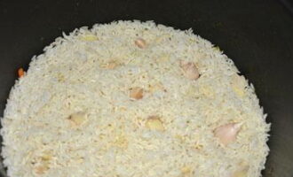 Peel the garlic and rinse in cold water. Make small depressions in the rice and place the peeled garlic in them.