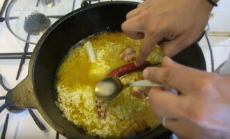 Spread the rice evenly over the entire surface using a slotted spoon. Place the previously peeled garlic and hot red pepper.