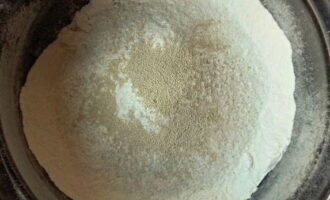 To prepare pizza dough with kefir, sift the flour into a deep bowl. Mix it with the rest of the dry products: soda, salt and sugar.