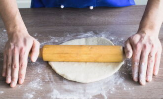 Dryss den ferdige deigen med en liten mengde mel slik at den ikke fester seg til bordet eller hendene. Bruk en kjevle og kjevle ut til en pen tynn bunn.