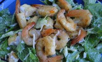 Dalam hidangan berasingan, satukan salad, udang dan crouton. Masukkan sos di sini dan kacau dengan dua sudu besar, berhati-hati agar tidak menumbuk sayur-sayuran dan udang. Taburkan salad dengan keju parut.