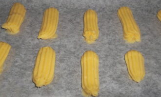 Cover the baking sheet with oiled parchment. We plant oblong eclairs of the desired length on it. We leave enough space between the pieces - the dough increases significantly in volume during baking.