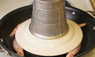 Placez un poids au fond de l'assiette. Il peut s'agir par exemple d'une pierre ou d'une petite casserole ou d'une bouilloire remplie d'eau. À ce stade, la tâche consiste à presser la carcasse autant que possible au fond de la poêle pour une friture uniforme et rapide. La température du poêle est moyenne-élevée.