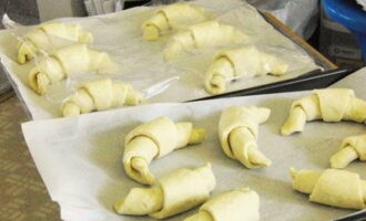 Place parchment paper on a baking sheet, onto which we place croissants made from puff pastry. Cover them with cling film and let them stand in a warm place for 30-40 minutes.