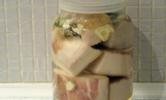 Place pieces of lard tightly into clean and dry jars, alternating them with garlic, bay leaves and black peppercorns. Fill with boiling water, close the lid and leave until cool. 