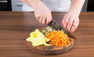 Netegeu la resta de verdures. Tallem les patates a làmines fines i ratllem les pastanagues. També piquem cogombres en escabetx.