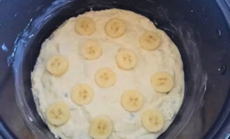 Carefully place the prepared curd dough into the multicooker bowl and level it with a silicone spatula. If desired, place banana slices on top.