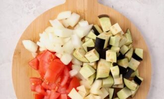 Peel the onion and finely chop. Wash the tomatoes and eggplants and cut them into cubes. Finely chop the greens with a knife.