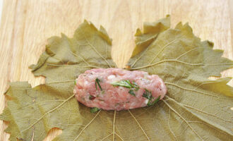 Coloque as folhas de uva com o lado liso voltado para baixo. Forme pequenas costeletas com a carne picada e coloque-as sobre as folhas.