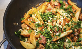 Place the fried potatoes in a frying pan with the meat and onions, and also add chopped garlic and chopped herbs to the ingredients.