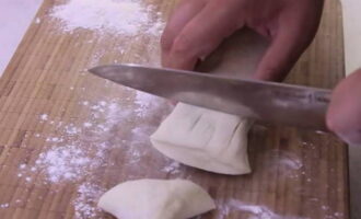 When the dough has settled, take it out of the container. Dust a wooden board with flour. Cut the dough into small pieces.Their size can vary depending on your desire. Keep in mind that as you bake the pies, they will increase in size. 