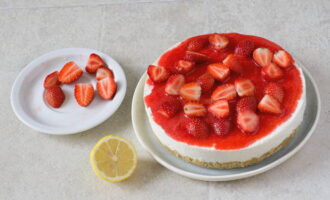 Nehmen Sie die Käsekuchenform nach sechs Stunden aus dem Kühlschrank und geben Sie den Inhalt in eine große Untertasse. In Scheiben geschnittene Erdbeeren auf die Quarkcreme legen und mit Erdbeerpüree füllen. Geschnittene Zitronenschale darüber streuen.