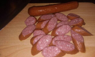 How to simply and deliciously cook pasta with sausages? Take your favorite sausages or those left in the refrigerator. It’s best to use hunting sausages in this dish; they will add a special smoky taste and smell. On a cutting board, cut them into elongated circles.