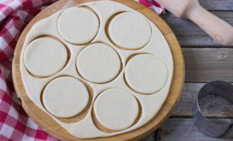 Then roll out the dough on a work surface, cut out round blanks for dumplings using a glass.