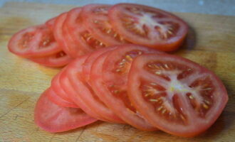 Wash the tomatoes in running water. Cut them into circles or slices. Pour the juice released from the eggplants into the sink and fill them with minced meat and herbs. Place tomatoes on top.