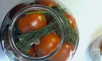 Place the tomatoes tightly in the jar, top them with sprigs of herbs and cloves of garlic.