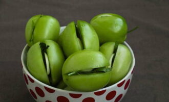 Haz un corte profundo en cada tomate. Coloca una ramita pequeña de perejil y una rodaja de ajo en el corte.