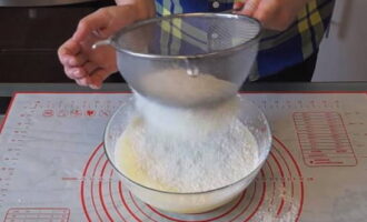 Next, add the sifted flour in parts and knead the dough. Add baking powder along with flour.