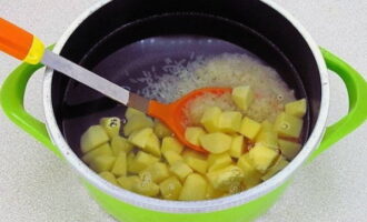 Pour water into a suitable size pan, bring to a boil and add potato cubes and rice. Cook over medium heat.