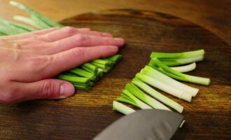 Let's do the greens. We cut off the white dense roots of the green onions, cut them lengthwise and lower them into the broth for a minute, and finely chop the green part.