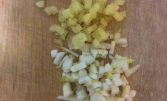 Using a sharp knife, very finely chop a piece of ginger and cloves of garlic.