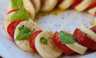 Bestrooi alles vervolgens met een beetje zout en gemalen zwarte peper. Besprenkel de salade met balsamicoglazuur of azijn en olijfolie.Op het einde versieren we alles met verse basilicumblaadjes.