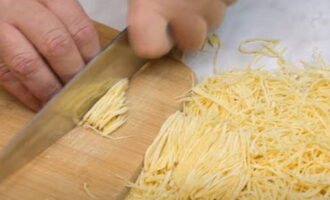 Let the rolled out layer dry, leaving it on the table for ten to fifteen minutes. Then generously sprinkle the surface of the layer with flour and roll it into a loose roll. Next, cut the roll crosswise. You can cut into thin strips - you get thin noodles. After cutting, distribute it with your hands on the table surface. 