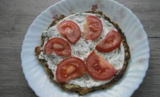 Laten we beginnen met het samenstellen van de taart. Leg de pannenkoek op een platte schaal, bestrijk hem met saus en voeg de in dunne halve ringen gesneden tomaten toe. Breng de vulling op smaak met gemalen zwarte peper.