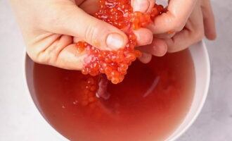 After this, carefully separate the caviar from the shell. Hold the film on one side and squeeze out the eggs with your fingers. Rinse the caviar 3-4 times under running water.