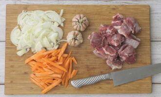 Rinse and dry the boneless lamb with a napkin. Then cut the meat into small cubes. Peel the onion and chop three onions into thin quarter rings. Chop the carrots into strips. Peel the garlic heads from the outer peel.