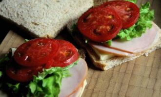 Place one slice of rye and white bread on the work surface, put two slices of ham and cheese, and top with thin slices of tomato and leaves of green lettuce - cover with the remaining pieces of bread.