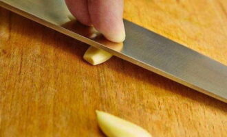 Peel the garlic and crush it with the flat side of the knife.