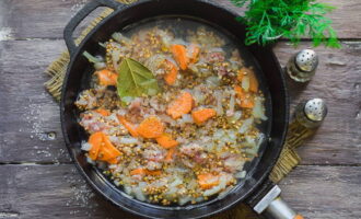 Giet een glas verwarmd, schoon water in de braadpan. Voeg vervolgens een laurierblad toe aan deze ingrediënten, voeg gemalen zwarte peper en zout naar smaak toe en meng alles. Bedek de koekenpan met een deksel. Laat de boekweit met gehakt op laag vuur 20-30 minuten sudderen. Roer tegen het einde van de bereiding het gerecht opnieuw door en neem een ​​monster.