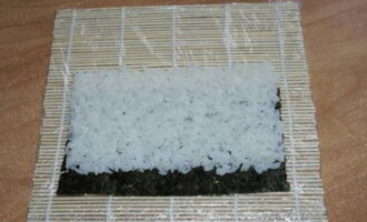 Using hands moistened with water and vinegar, lay the prepared rice in an even layer and, without pressing too hard, leaving the edge of the nori for overlap.