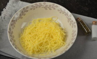 Grate a piece of cheese using a fine-hole grater into a separate deep container, such as a plate or bowl.