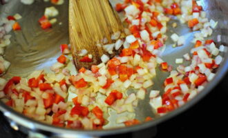 Place the cooked ribs from the pan onto a plate. Wash the bell pepper and remove its stem with a knife. Then cut the fruit in half to remove the core. Cut the pepper and pre-peeled onion into small cubes. Place the vegetables in the pan with the remaining oil and pork fat. Sauté them for 10 minutes until soft.