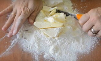 How to bake a classic onion pie at home? Sift the required amount of wheat flour onto the work surface of the table. Add cold butter to it and chop it with a knife until it becomes fine crumbs.