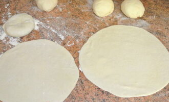 Now divide the dough into small pieces and roll each into balls. Roll out flat cakes from each using a rolling pin, then cover them with a towel so that they do not dry out while the potatoes are boiling.