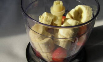 Next, take the banana slices out of the freezer and place them in a blender bowl along with a handful of washed strawberries.