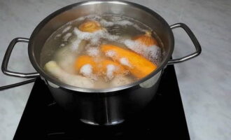 Wash the onion well and add it to the pan with the chicken. Next, put the peeled carrots there, pour in about 1.5 liters of water, put it on the fire, bring the broth to a boil and skim off the resulting foam.