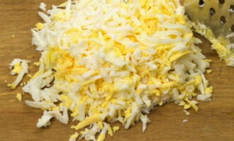 Grate the boiled eggs on a coarse grater, leaving two yolks for decoration.