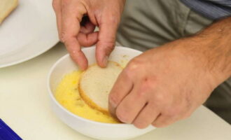 Despeje o óleo vegetal na frigideira. Coloque o recipiente no fogão aceso e, enquanto o óleo esquenta, enfie as fatias de pão em um garfo e mergulhe-as uma a uma na mistura de ovos e leite.