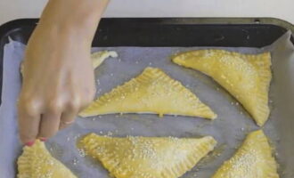 Preheat the oven (set the temperature to 200 degrees). Line the bottom of a baking tray with baking paper. Lay out the pies. Place the baking sheet with the preparations in the refrigerator for 10 minutes. Brush the pies with the remaining egg yolk. Pierce with a fork in several places. Sprinkle the preparations with sesame seeds.