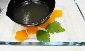 Cut the boiled carrots into slices and place them in a form for jellied meat. Then put parsley there, pour one ladle of cooled broth and put it in the refrigerator for 10-15 minutes. This will be the top of the jellied meat.