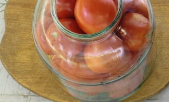 Kami meletakkan tomato dalam balang dengan longgar: kami cuba meletakkan buah yang lebih kecil di atas yang lebih besar. Goncangkan bekas supaya tomato sesuai dengan rapat.